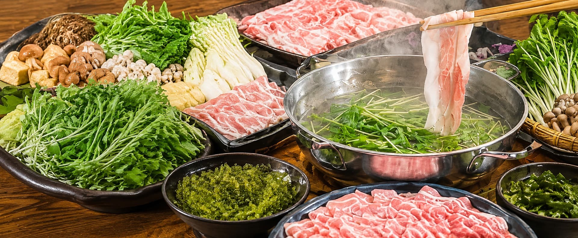 箸であぐー豚を持ち上げた、湯気の立つしゃぶしゃぶ鍋